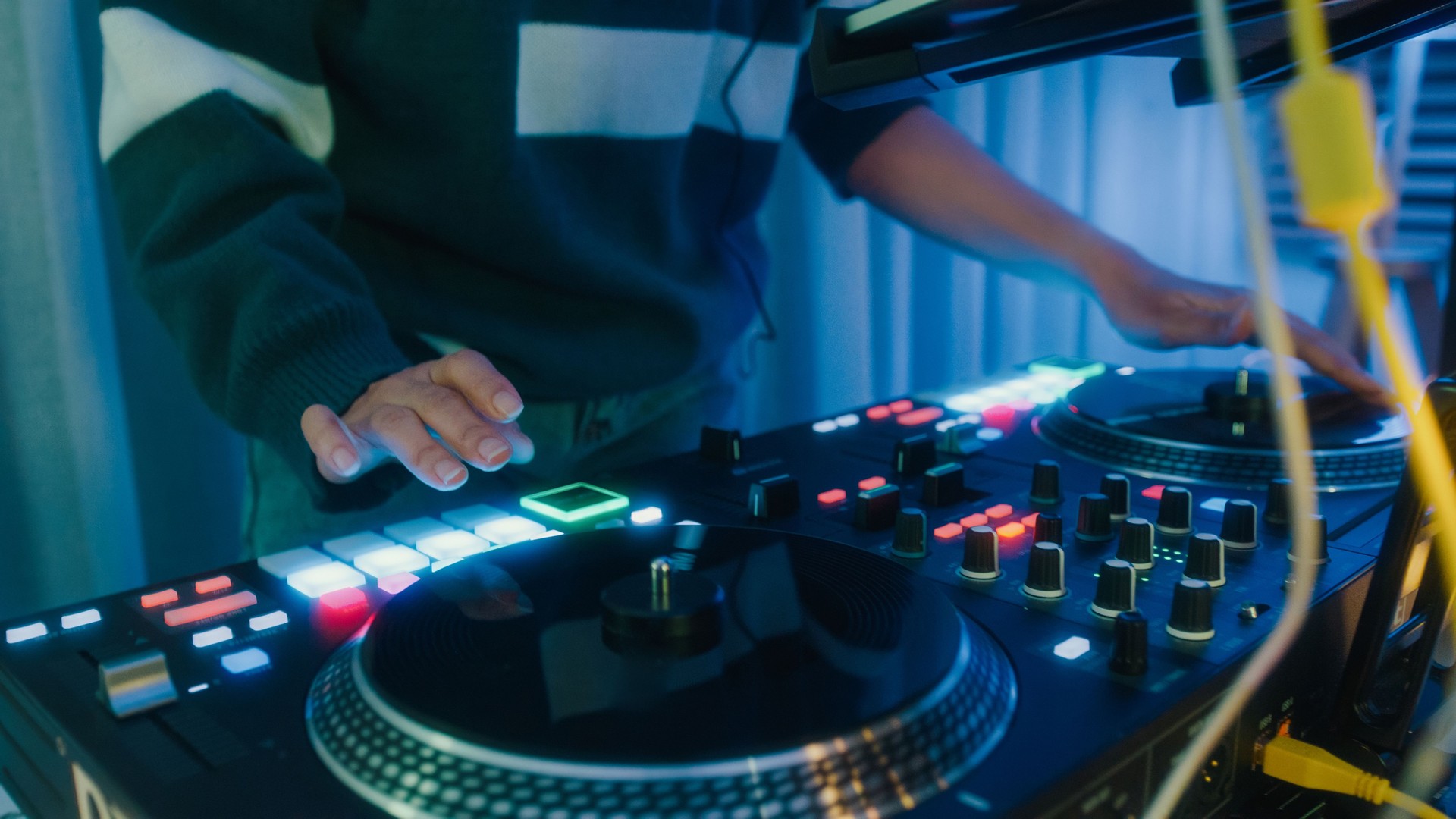 Young Asian woman dj girl playing music and scratching tracks on professional dj midi controller at colorful house party at night. Multicultural friend having fun together college house party.