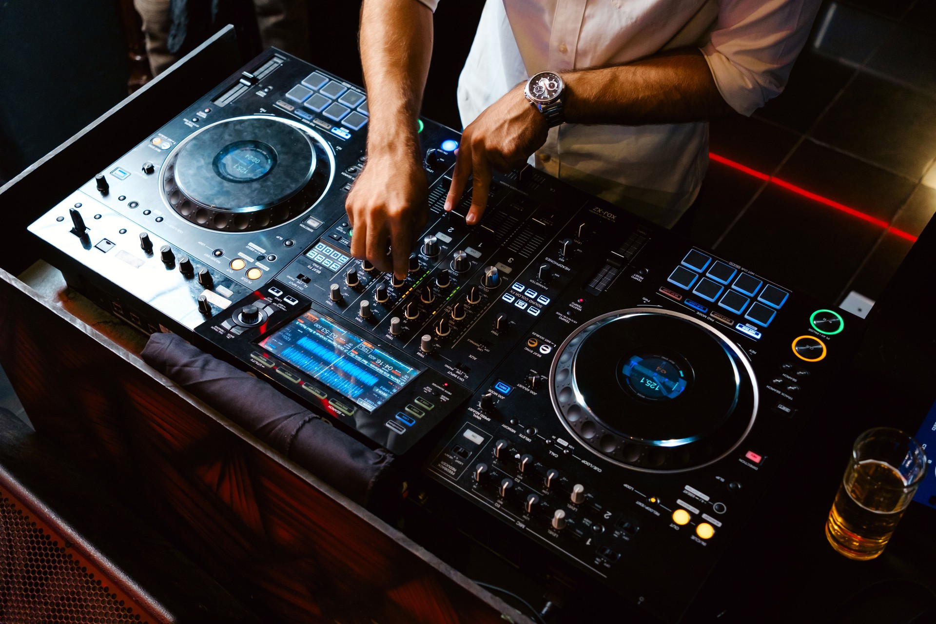 A DJ skillfully mixes music on a professional DJ controller at a nightclub. The illuminated soundboard, buttons, and turntables create a dynamic atmosphere for an exciting party experience.